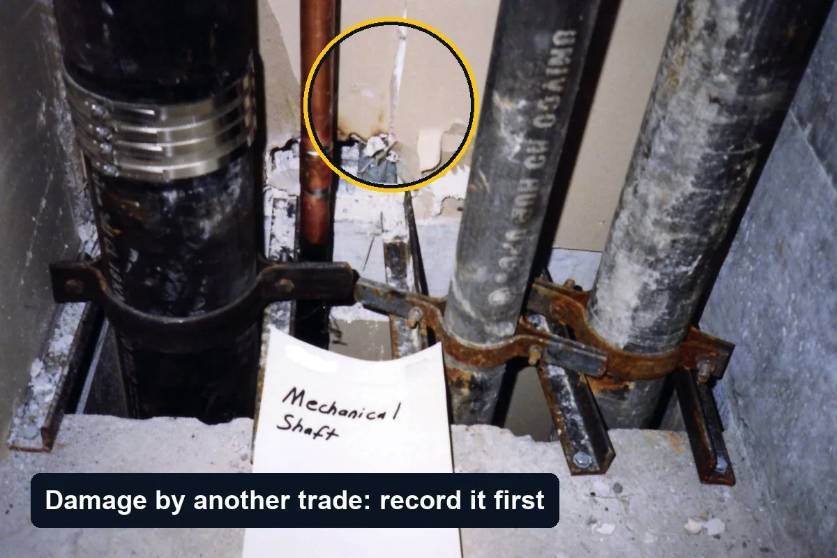Pipes in a mechanical shaft with broken drywall around them; the damaged board edge is circled with the label Damage by another trade: record it first