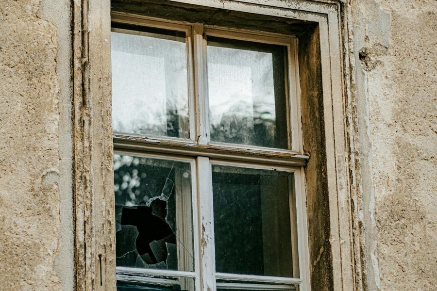Old timber window with a broken pane, cracked render around the reveal and a stained cill