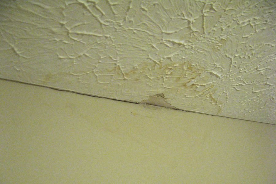 Textured ceiling with a brown water stain and cracking concentrated along the junction with the wall