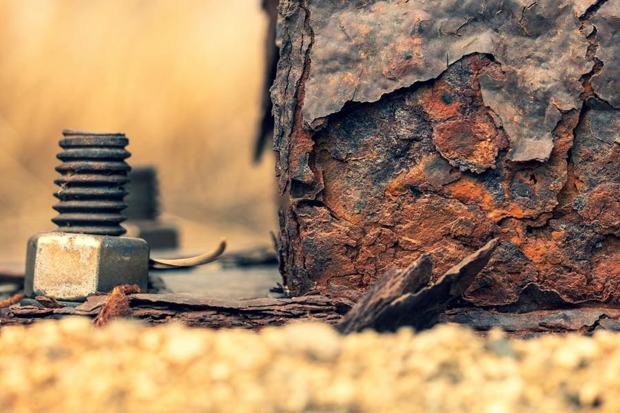 Heavily corroded steel column base with a rusted anchor bolt on a concrete pad