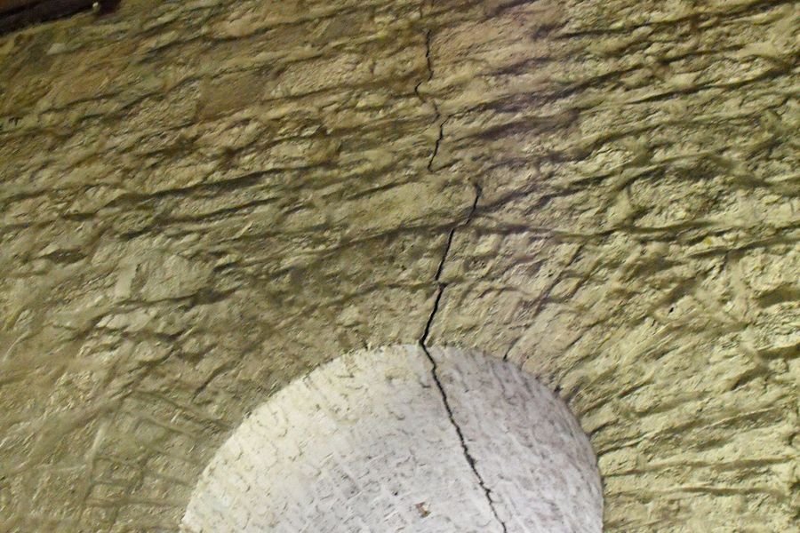 Vertical crack rising from the crown of an arched window opening through rubble stone masonry