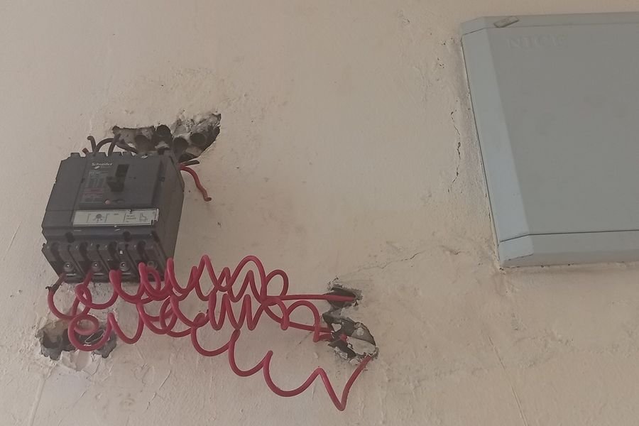 Electrical device fixed to a wall with a coiled red cable hanging loose from it, beside a closed consumer unit