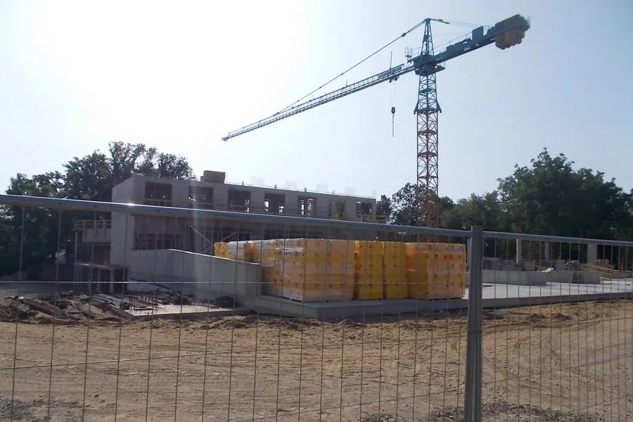 A hotel under construction with a tower crane, pallets of blocks and site fencing in the foreground