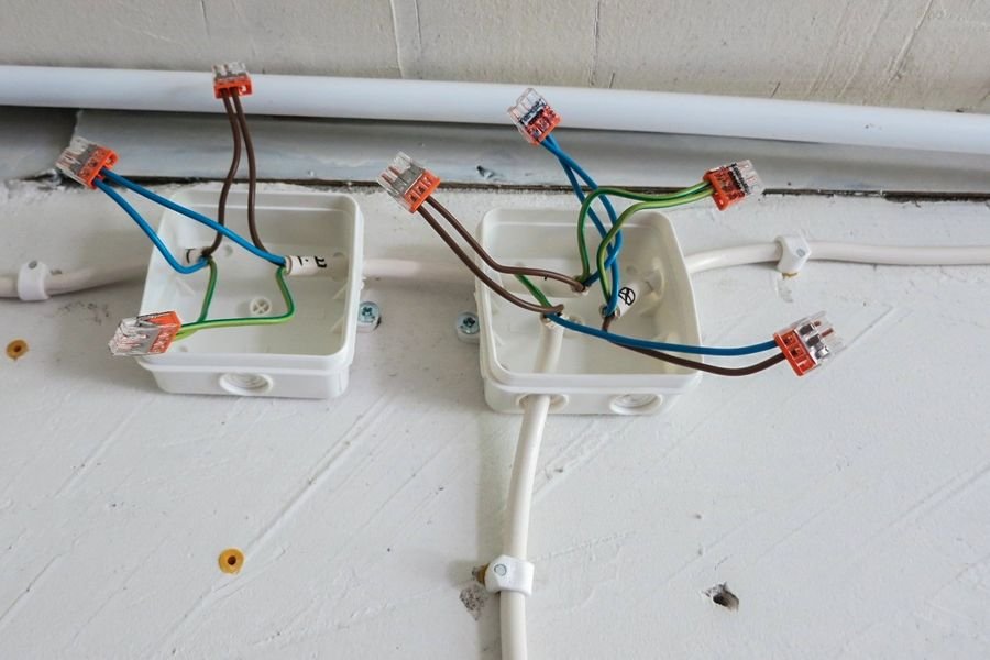 Two surface-mounted junction boxes on a wall with their lids off, cables entering and lever connectors exposed
