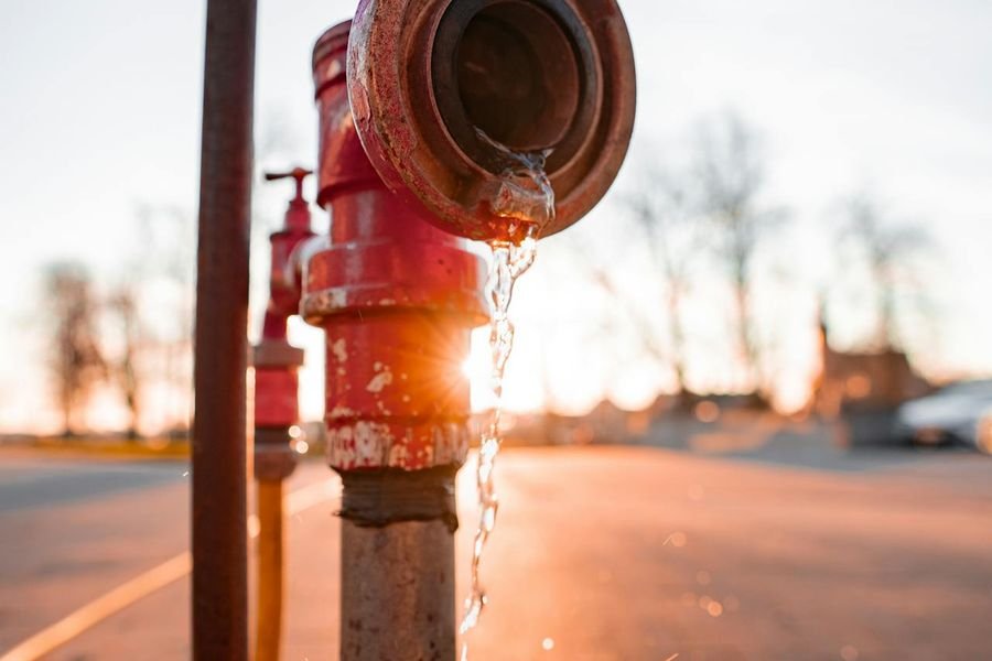Red external standpipe valve leaking water from its cap, against a low sun
