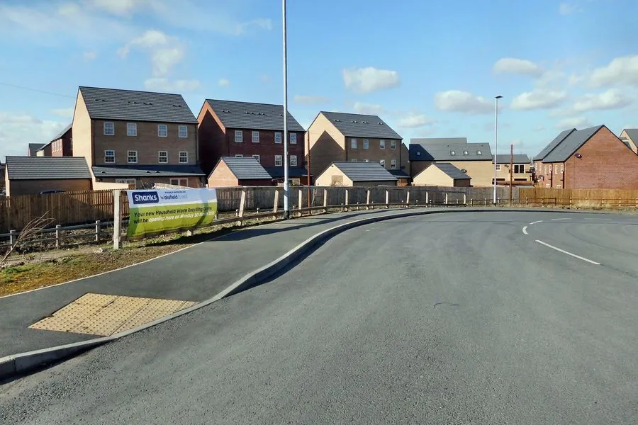A new housing estate in England with a finished road, a developer's sign and recently completed brick houses