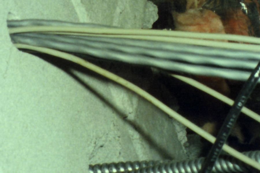 Cables passing through an oversized hole in a concrete block wall with loose fibreglass insulation pushed around them
