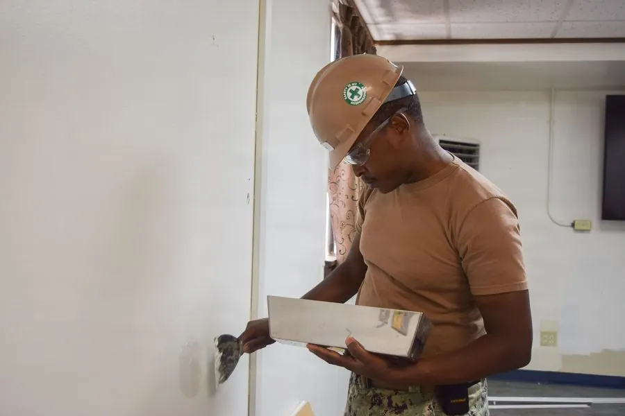 A worker in a hard hat filling and finishing a wall beside a doorway during an office renovation