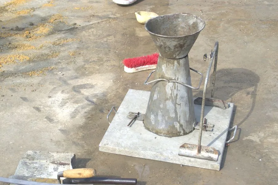 A slump cone, tamping rod and base plate on a concrete deck after a slump test
