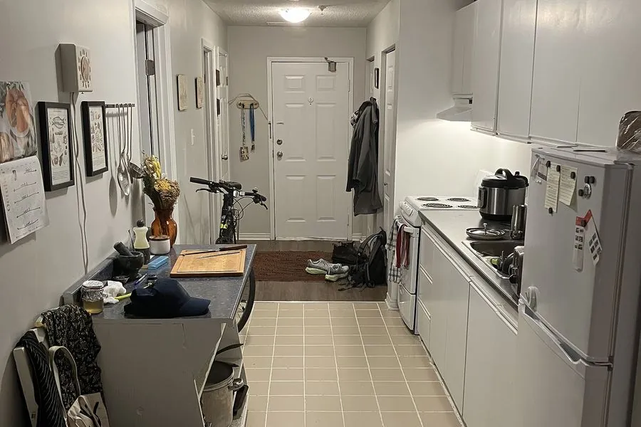 A long galley kitchen in a rented apartment with white units, a tiled floor and signs of wear