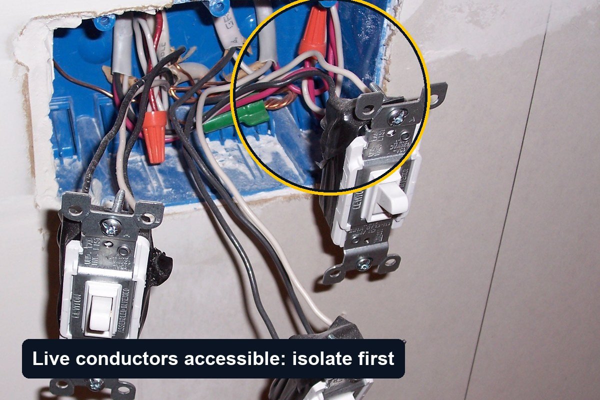 Three light switches hanging out of an open wall box on their cables, with bare conductor ends and wire connectors visible inside the box