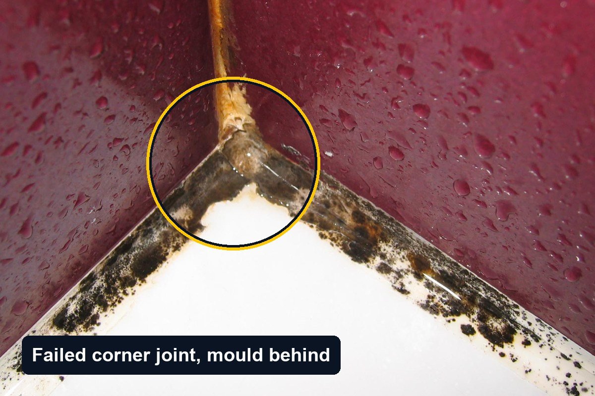 Internal corner of a shower with dark red tiles, water droplets on the tiles and black mould along the failed corner joints at the wall junction and the tray