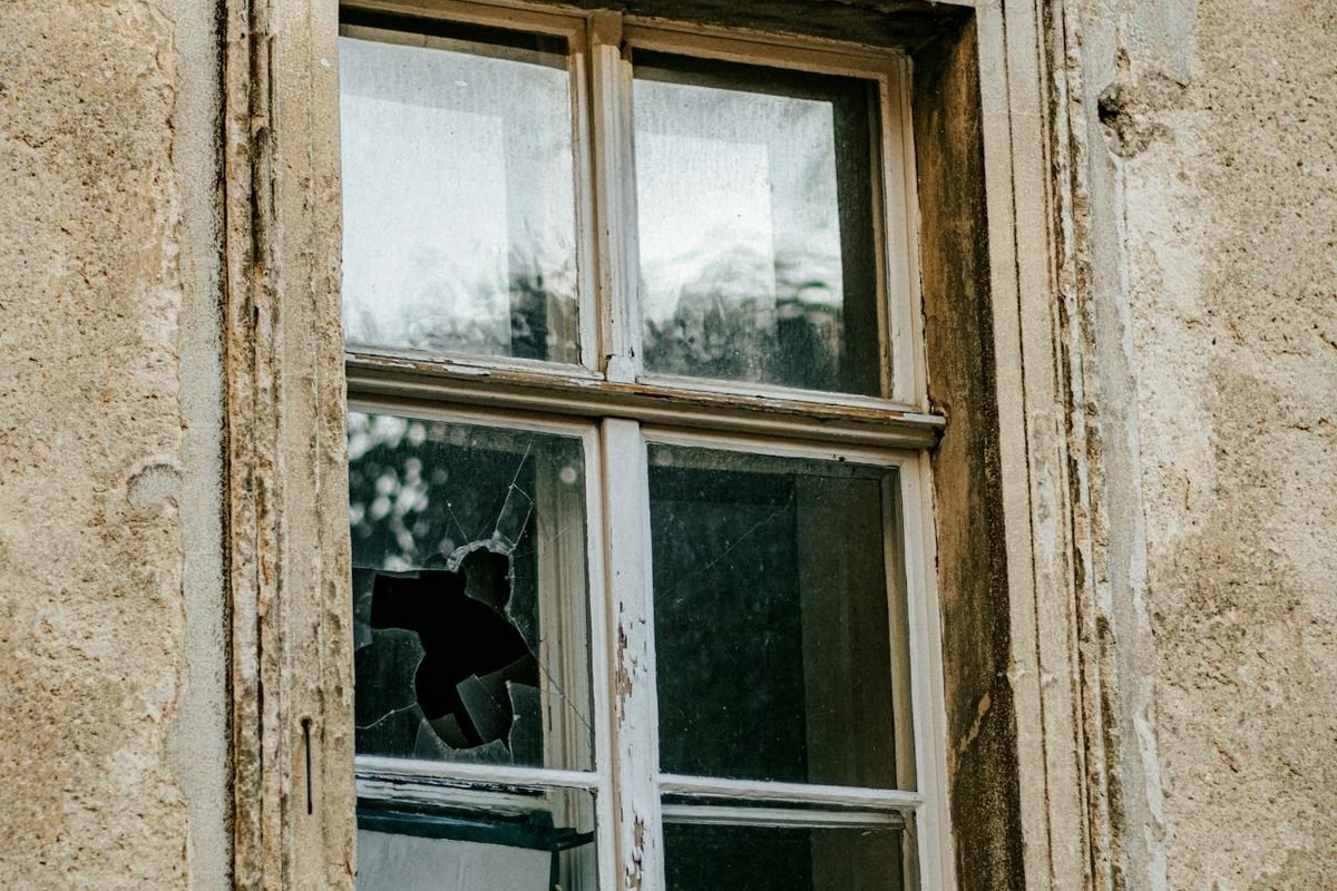 Old timber window with a broken pane, cracked render around the reveal and a stained cill