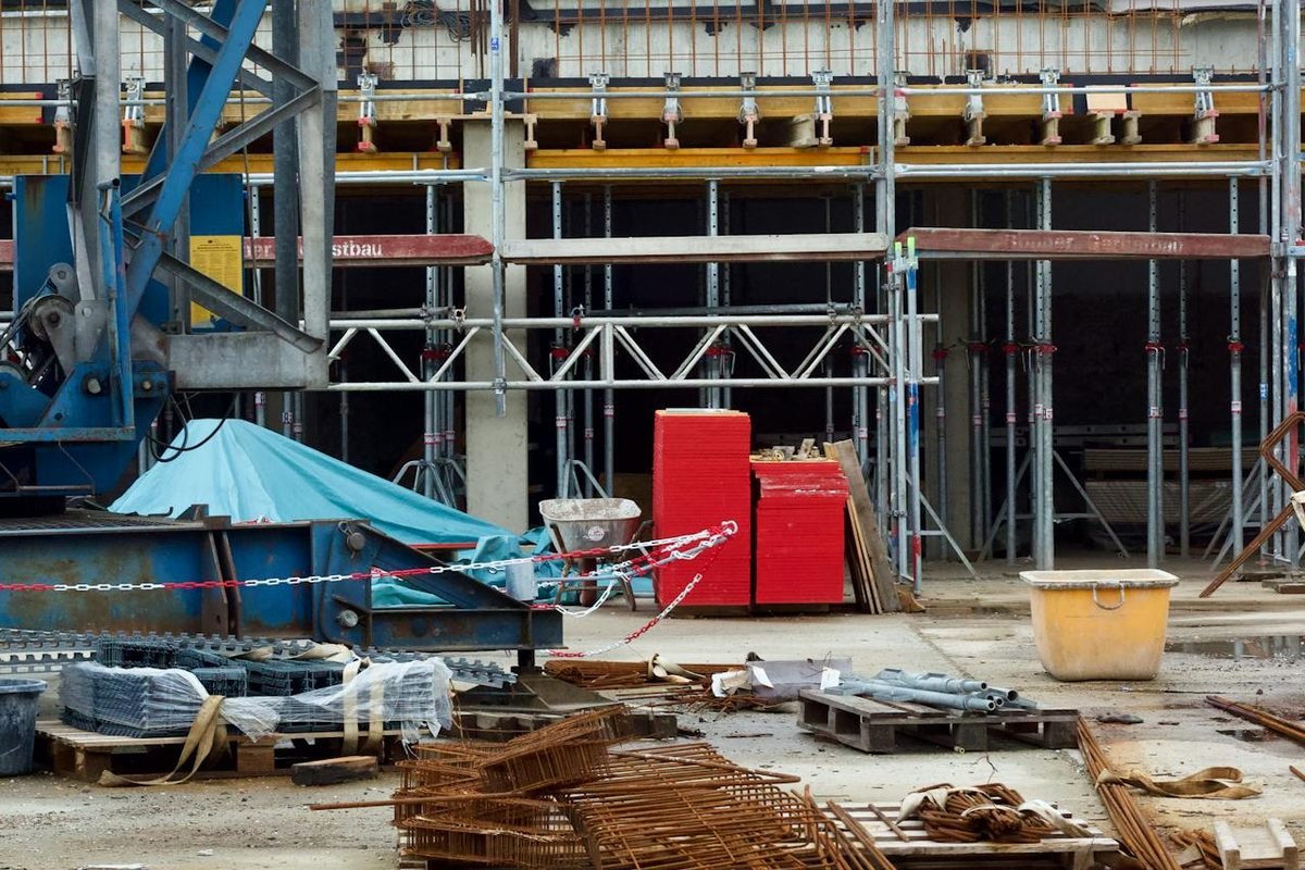 New-build construction site with scaffolding, a crane, stacked steel reinforcement and standing water