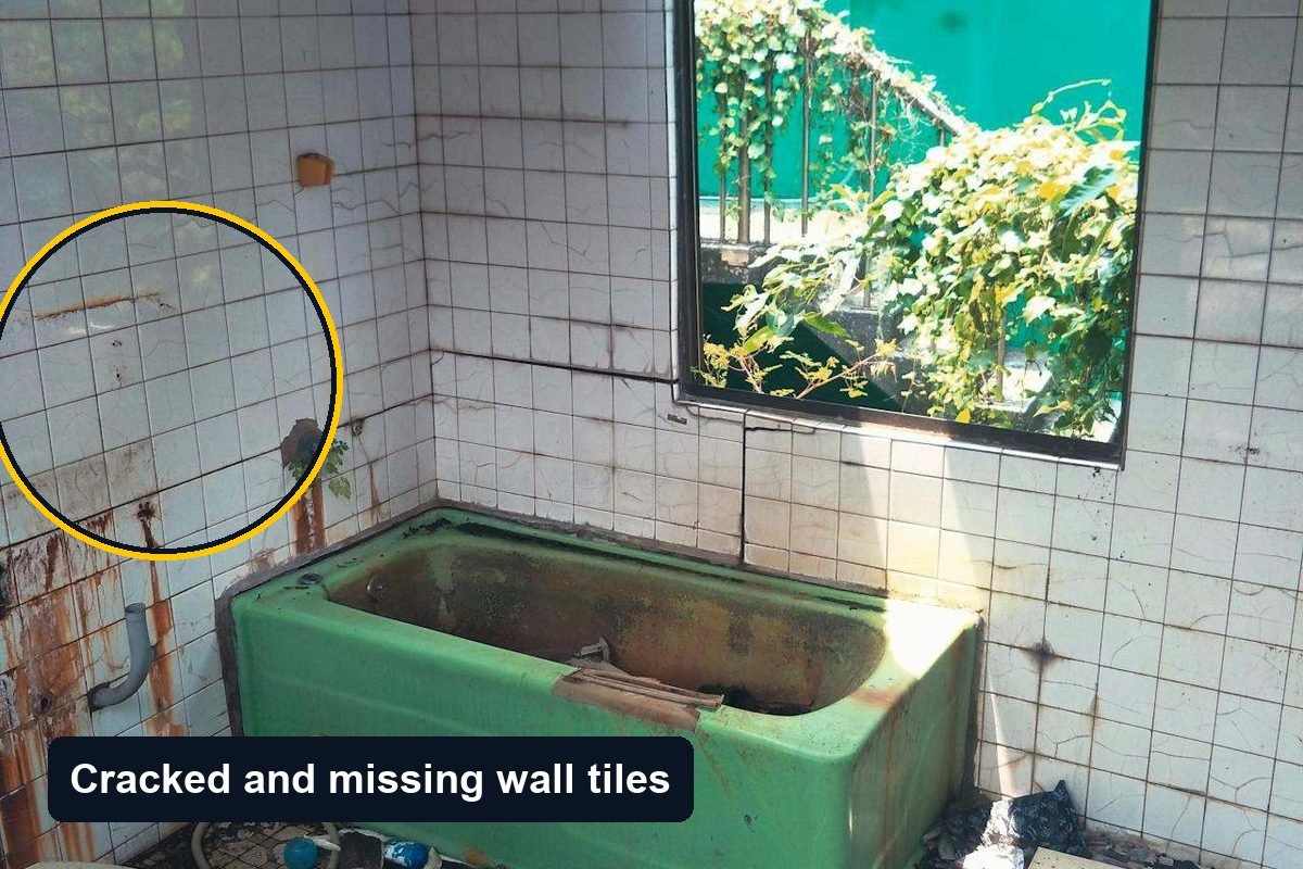 Derelict bathroom with cracked and missing wall tiles, a rusted bath and debris on the floor